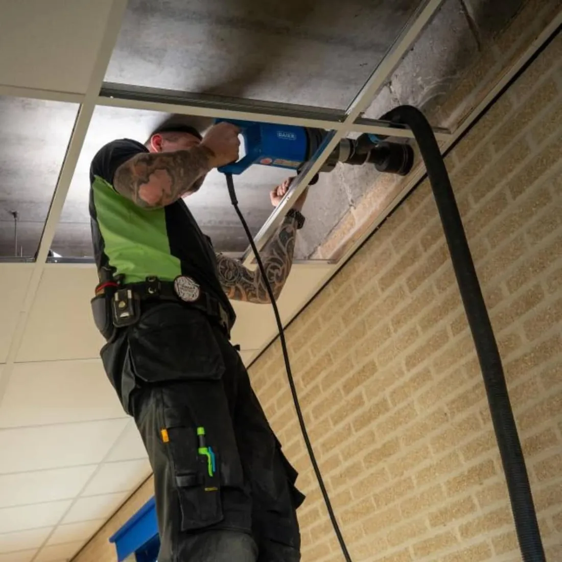 Monteur boort een kerngat door het plafond voor het leidingwerk